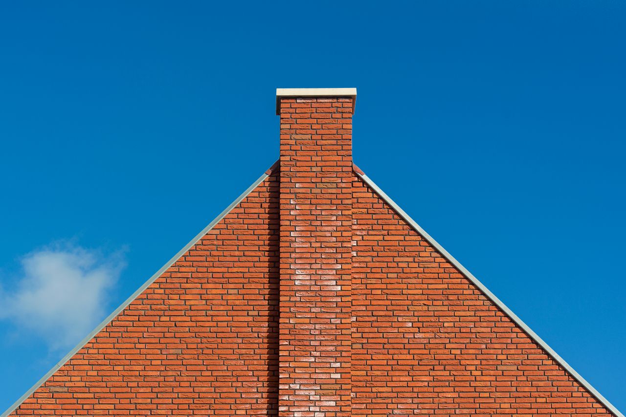 Red brick wall with chimney against clear blue sky, emphasizing architectural design.