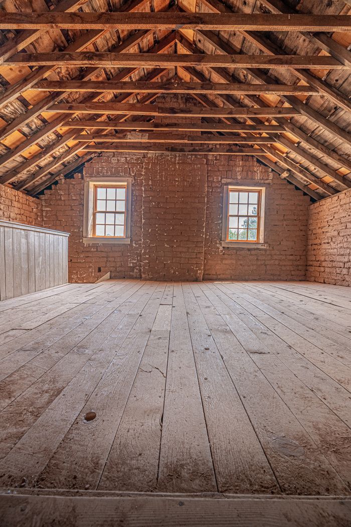 Spacious attic interior featuring exposed wooden beams and brick walls, perfect for renovation or design inspiration.
